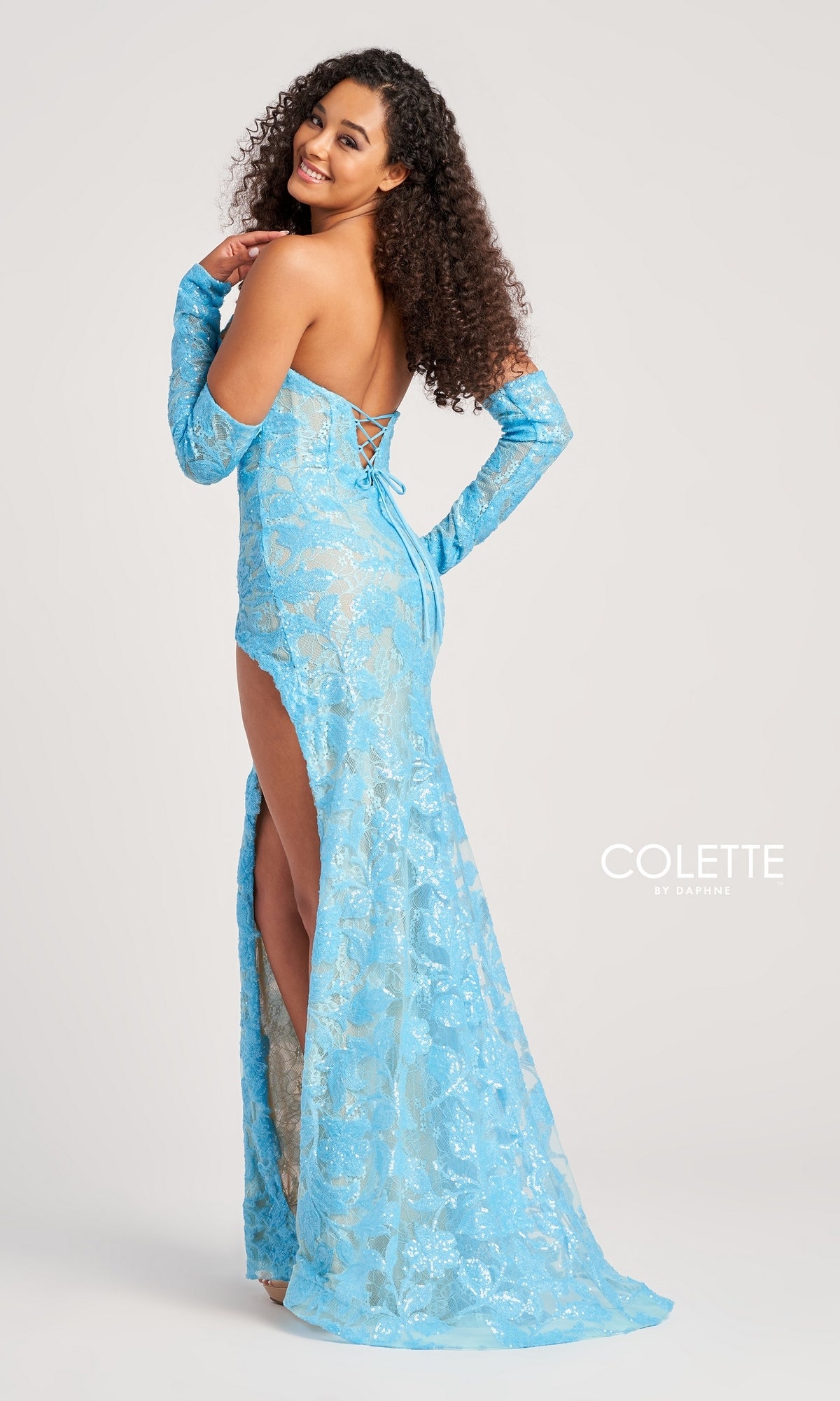Woman wearing the Colette Strapless Prom Dress with Gloves CL5107—a light blue sequin gown with a high slit, matching gloves, and back lace-up detail—stands sideways smiling, radiating elegance.